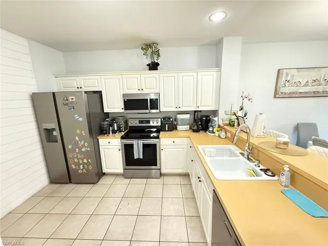Kitchen with stainless steel appliances, light countertops, white cabinets, light tile patterned flooring, and a peninsula