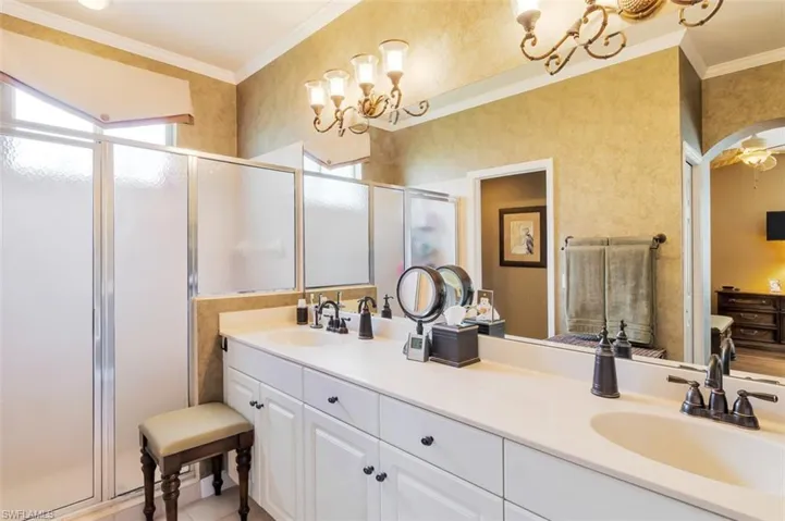 Bathroom featuring a chandelier, ornamental molding, walk in shower, and dual bowl vanity