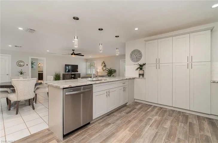 Kitchen with white cabinetry, dishwasher, sink, hanging light fixtures, and light wood-look tile