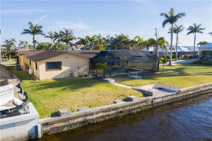 Back of property with stucco siding, a water view, glass enclosure, and a lawn