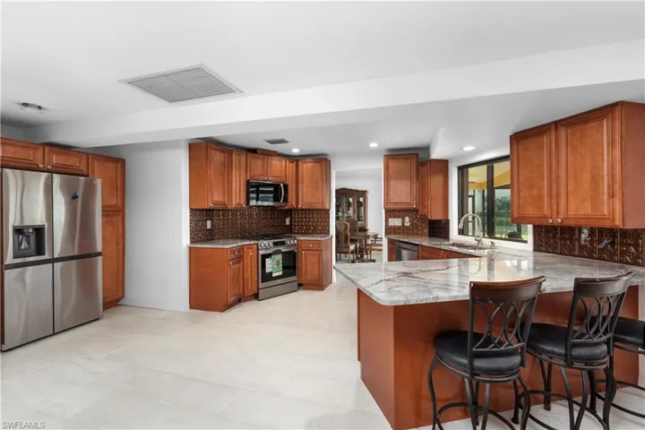Kitchen featuring visible vents, a peninsula, appliances with stainless steel finishes, a sink, and light stone counters