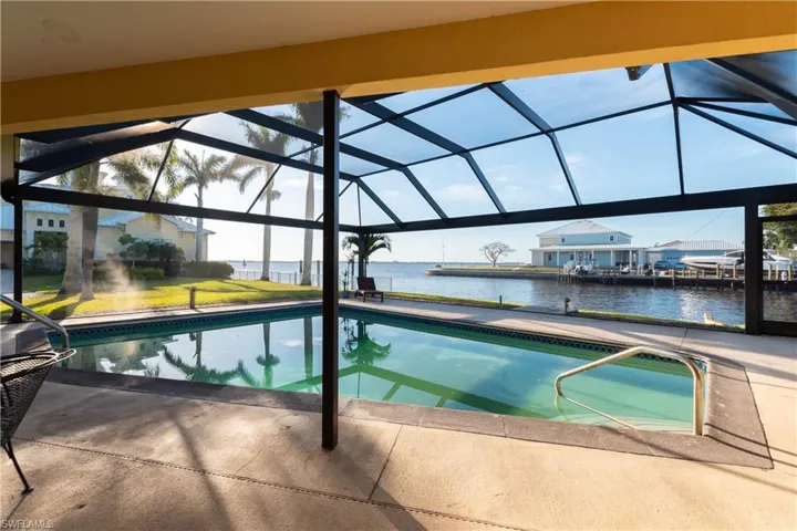 Outdoor pool with glass enclosure, a water view, and a patio area