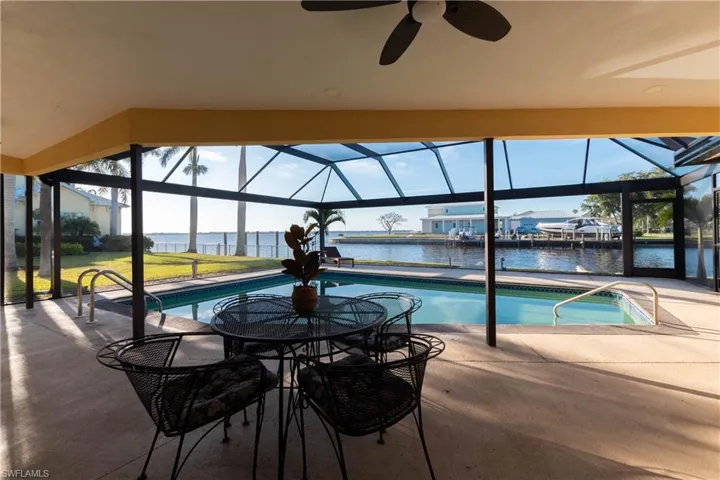 Outdoor pool with a lanai, a patio, a water view, a ceiling fan, and a lawn