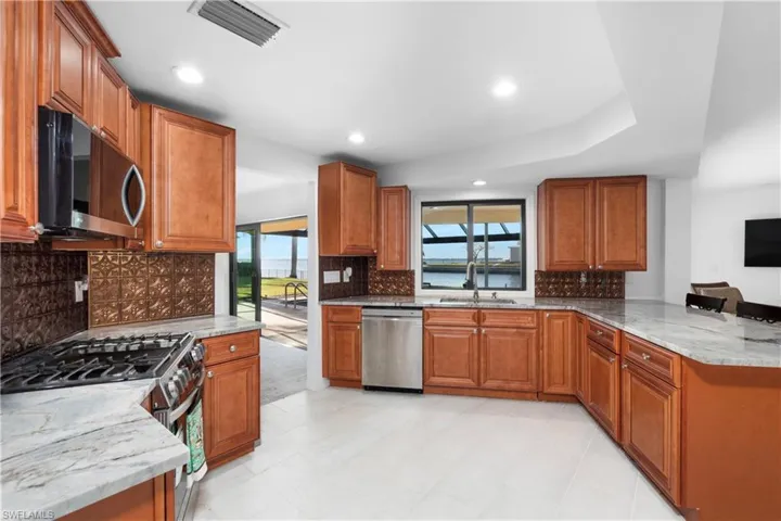 Kitchen featuring stainless steel appliances, a sink, visible vents, light stone countertops, and brown cabinets