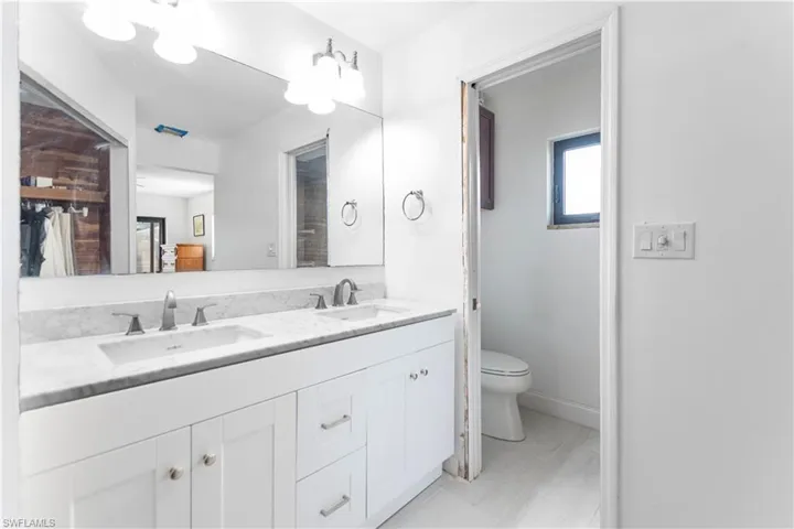 Bathroom featuring baseboards, double vanity, a sink, and toilet