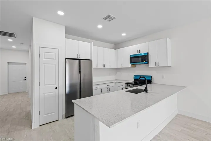 Kitchen with stainless steel appliances, white cabinetry, light stone countertops, light wood finished floors, and a peninsula