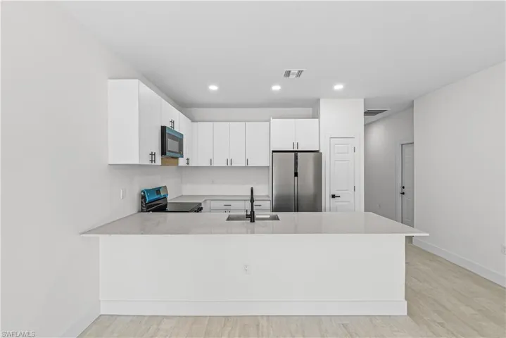Kitchen with white cabinetry, a peninsula, freestanding refrigerator, light wood-type flooring, and electric range