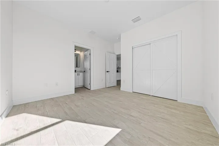 Unfurnished bedroom with light wood finished floors, connected bathroom, and a closet