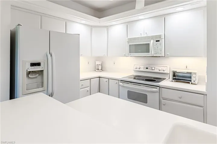 Kitchen featuring white appliances, light countertops, white cabinetry, and recessed lighting