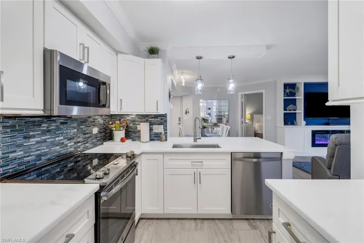 Kitchen featuring hanging light fixtures, sink, crown molding, white cabinetry, and appliances with stainless steel finishes