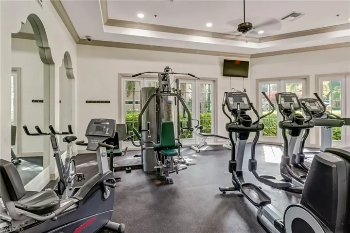 Gym with ornamental molding, a raised ceiling, and ceiling fan
