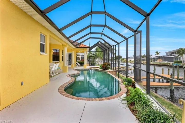 View of swimming pool featuring glass enclosure, a dock, a water view, and a patio
