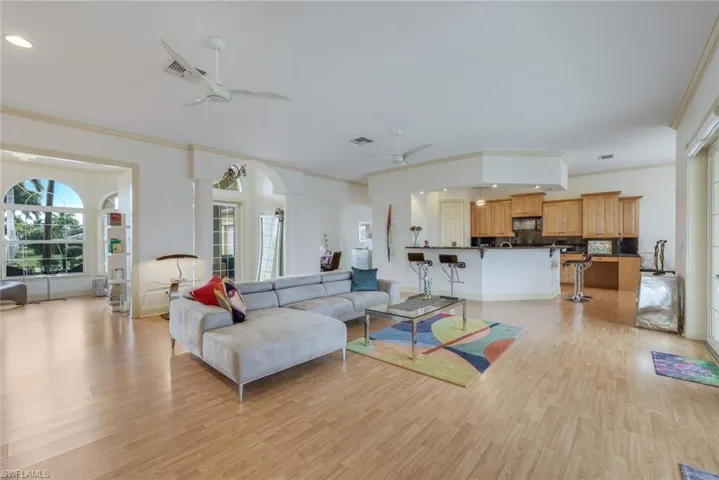Living room featuring ornate columns, ceiling fan, ornamental molding, and light wood-type flooring