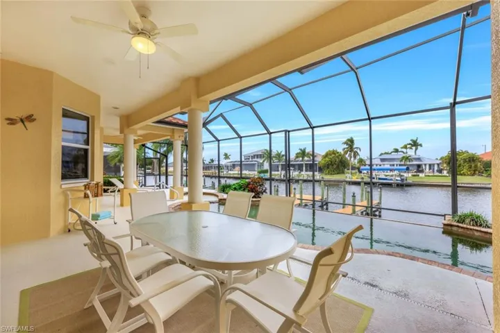 View of patio featuring glass enclosure, ceiling fan, a water view, and a boat dock