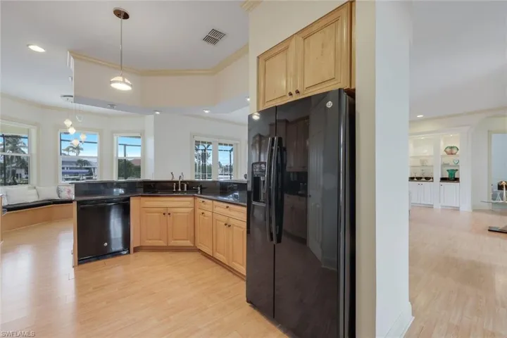 Kitchen with light wood-type flooring, ornamental molding, black appliances, light brown cabinets, and hanging light fixtures
