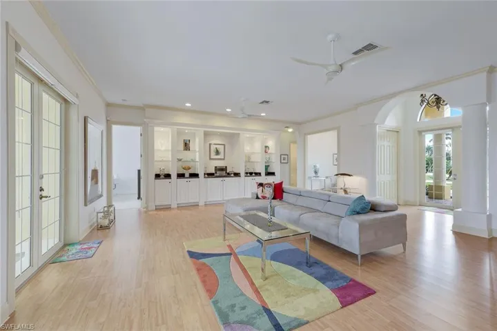 Living room with built in shelves, ceiling fan, french doors, crown molding, and light wood-type flooring