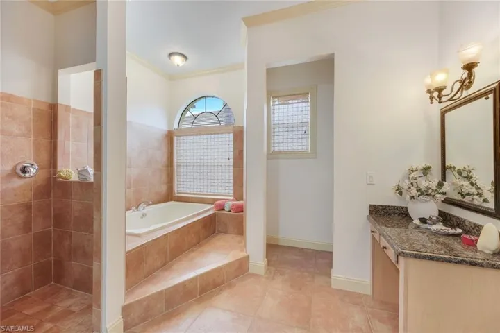 Bathroom featuring tile patterned flooring, vanity, tiled bath, and crown molding