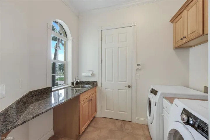 Laundry room with sink, light tile patterned flooring, washer and clothes dryer, crown molding, and cabinets