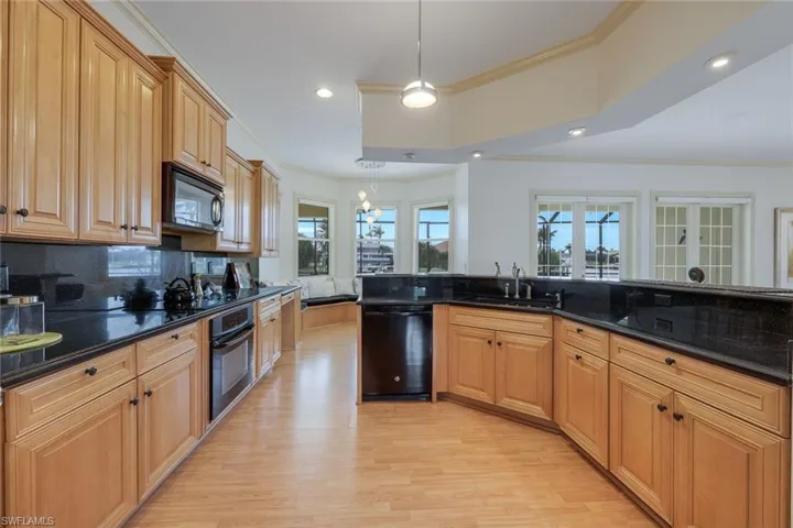 Kitchen featuring sink, light hardwood / wood-style flooring, pendant lighting, black appliances, and ornamental molding