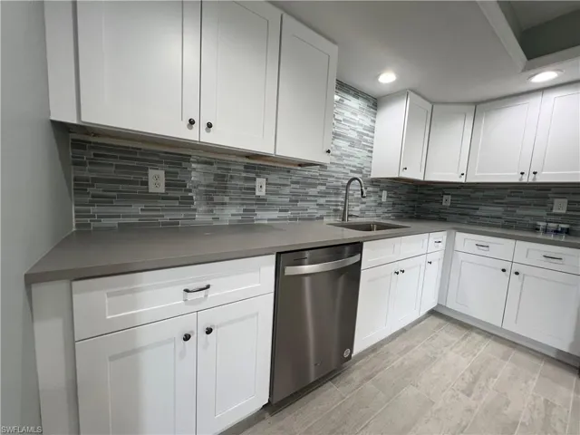 Kitchen with sink, backsplash, stainless steel dishwasher, light wood-type flooring, and white cabinetry