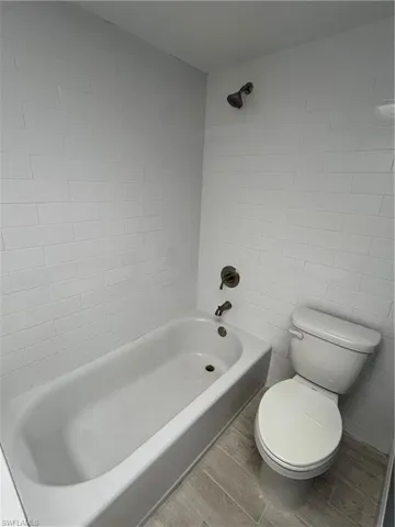 Bathroom with tile walls, tiled shower / bath combo, hardwood / wood-style flooring, and toilet