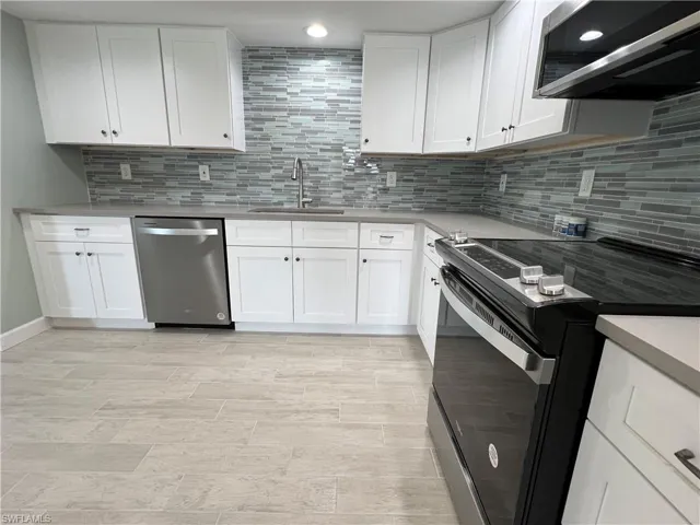 Kitchen featuring white cabinetry, range hood, decorative backsplash, and stainless steel appliances