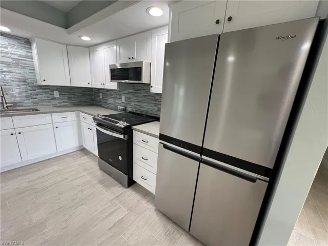 Kitchen featuring sink, stainless steel appliances, backsplash, and white cabinetry