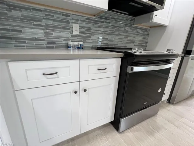 Kitchen with range hood, tasteful backsplash, light wood-type flooring, and stainless steel electric range oven