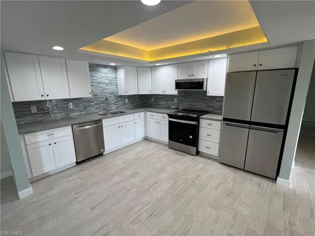 Kitchen with backsplash, a raised ceiling, appliances with stainless steel finishes, and sink
