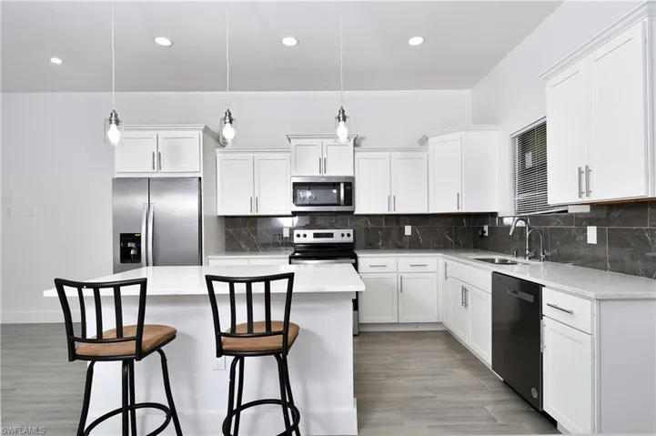 Kitchen with stainless steel appliances, pendant lighting, white cabinetry, and light wood-style floors
