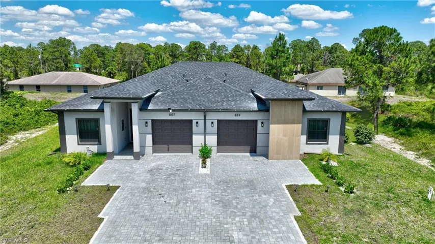 View of front of property featuring an attached garage, decorative driveway, a shingled roof, stucco siding, and a front lawn