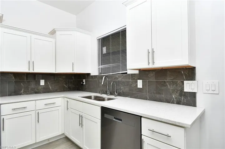 Kitchen featuring dishwasher, white cabinetry, light stone counters, and tasteful backsplash