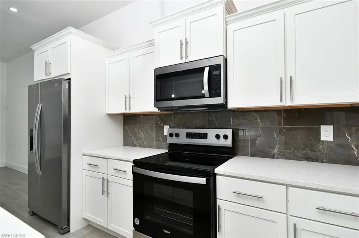 Kitchen featuring stainless steel appliances, white cabinets, light stone countertops, backsplash, and light wood-style flooring
