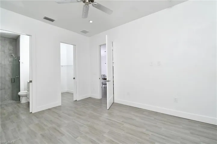 Unfurnished bedroom featuring a spacious closet, a ceiling fan, connected bathroom, and light wood finished floors
