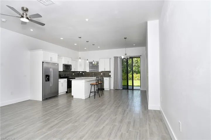 Kitchen with stainless steel appliances, a breakfast bar, white cabinetry, suspended lighting, and a kitchen island
