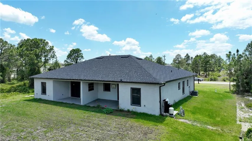 Back of house featuring a yard, a patio, stucco siding, and a shingled roof