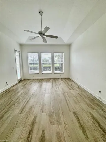 Unfurnished room featuring light wood-style floors, a ceiling fan, and a tray ceiling