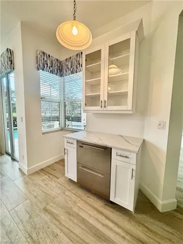 Bar featuring white cabinetry, light stone countertops, dishwashing machine, and hanging light fixtures