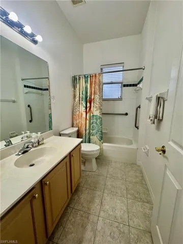 Full bath featuring vanity, shower / bathtub combination with curtain, and light tile patterned floors