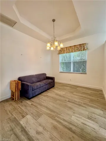 Sitting room featuring hanging lights, a raised ceiling, and light wood-type flooring