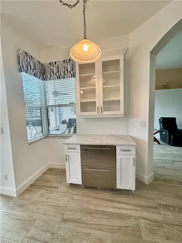Bar area with white cabinets, hanging light fixtures, glass fronted cabinets, light stone countertops, and stainless steel dishwasher
