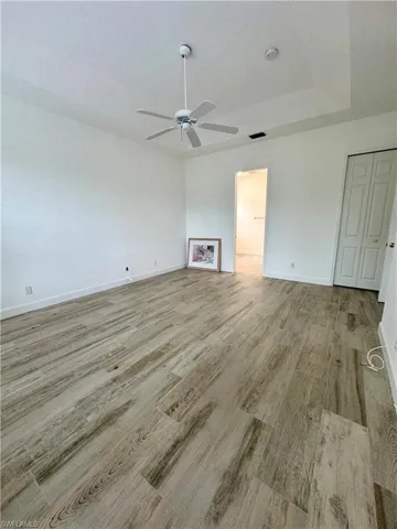 Unfurnished living room with light wood finished floors, ceiling fan, and a tray ceiling