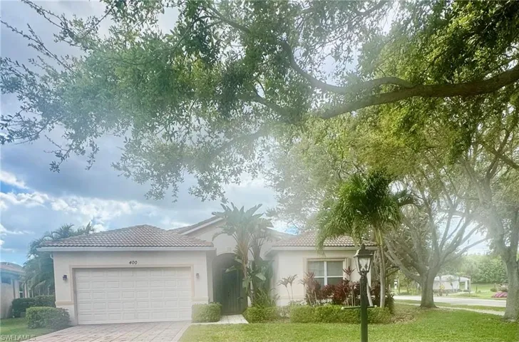 View of front facade featuring a tiled roof, a garage, stucco siding, and a front lawn