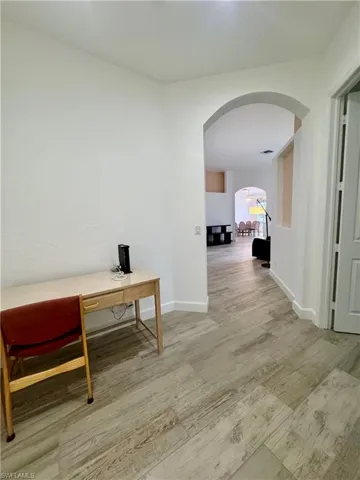 Hall with light wood-style floors, a desk, and arched walkways