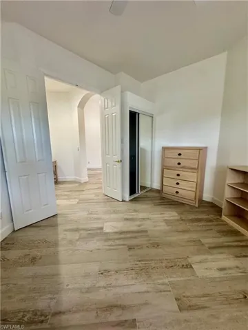 Unfurnished bedroom featuring arched walkways, light wood-type flooring, a closet, and a ceiling fan