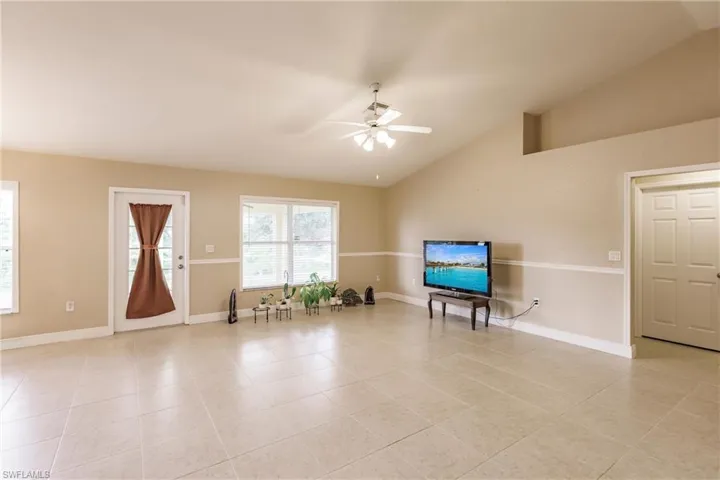 Living area featuring vaulted ceiling, light tile patterned floors, and ceiling fan
