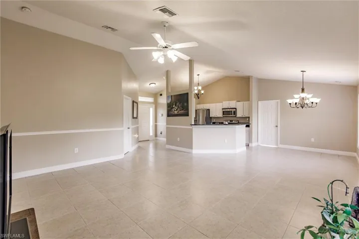 Unfurnished living room featuring ceiling fan with notable chandelier, light tile patterned floors, and high vaulted ceiling