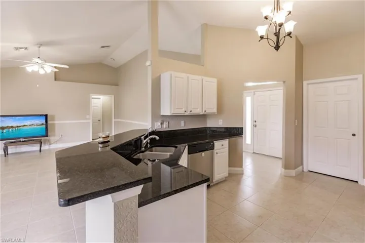 Kitchen with stainless steel dishwasher, white cabinetry, kitchen peninsula, ceiling fan with notable chandelier, and light tile patterned floors