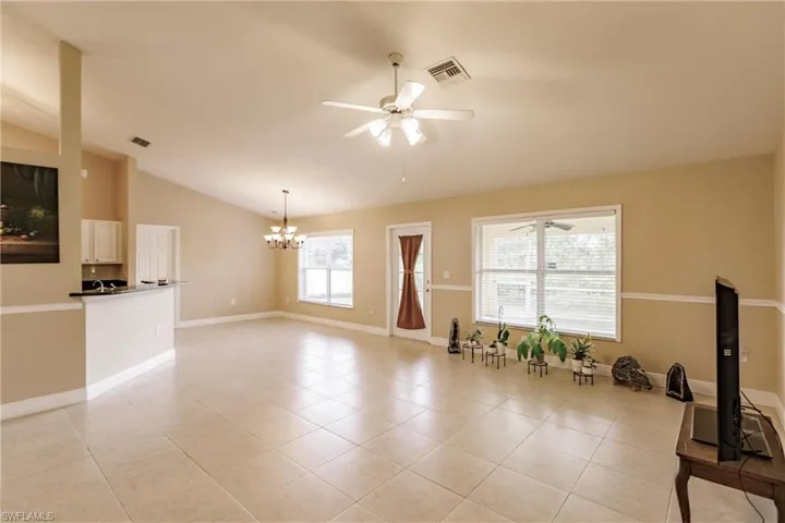 Tiled living room featuring ceiling fan with notable chandelier and lofted ceiling