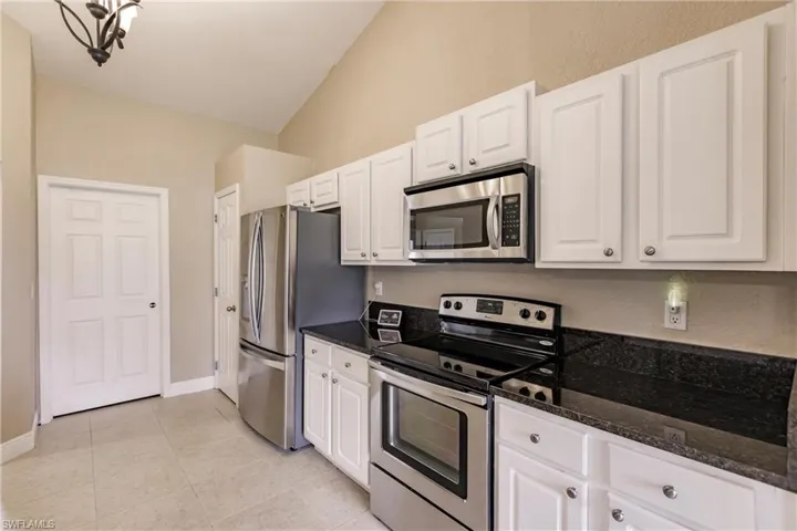 Kitchen with appliances with stainless steel finishes, dark stone counters, lofted ceiling, and white cabinetry